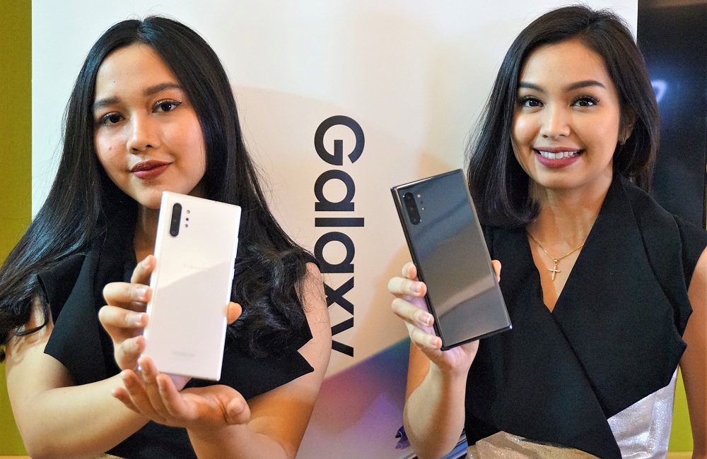 Sepasang model sedang memamerkan dua varian Samsung Galaxy Note 10 berbeda.