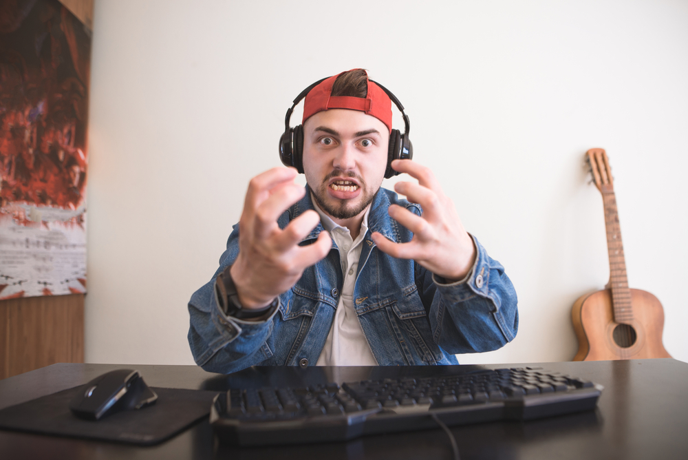 Portrait of an emotional gamer with headphones and a beard behind the game at home video games. Angry man playing games at home in a room and looking at the camera. Gamer is angry because he has lost for SEO
