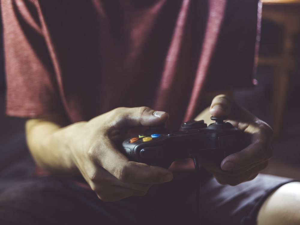 bearded man holding video game joystick controller in hands in front of body at home in the night for SEO